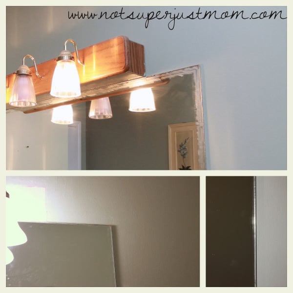 The bare bathroom mirror above the vanity after the old glued-on frame and its glue residue were scraped away, with a new light fixture mounted above